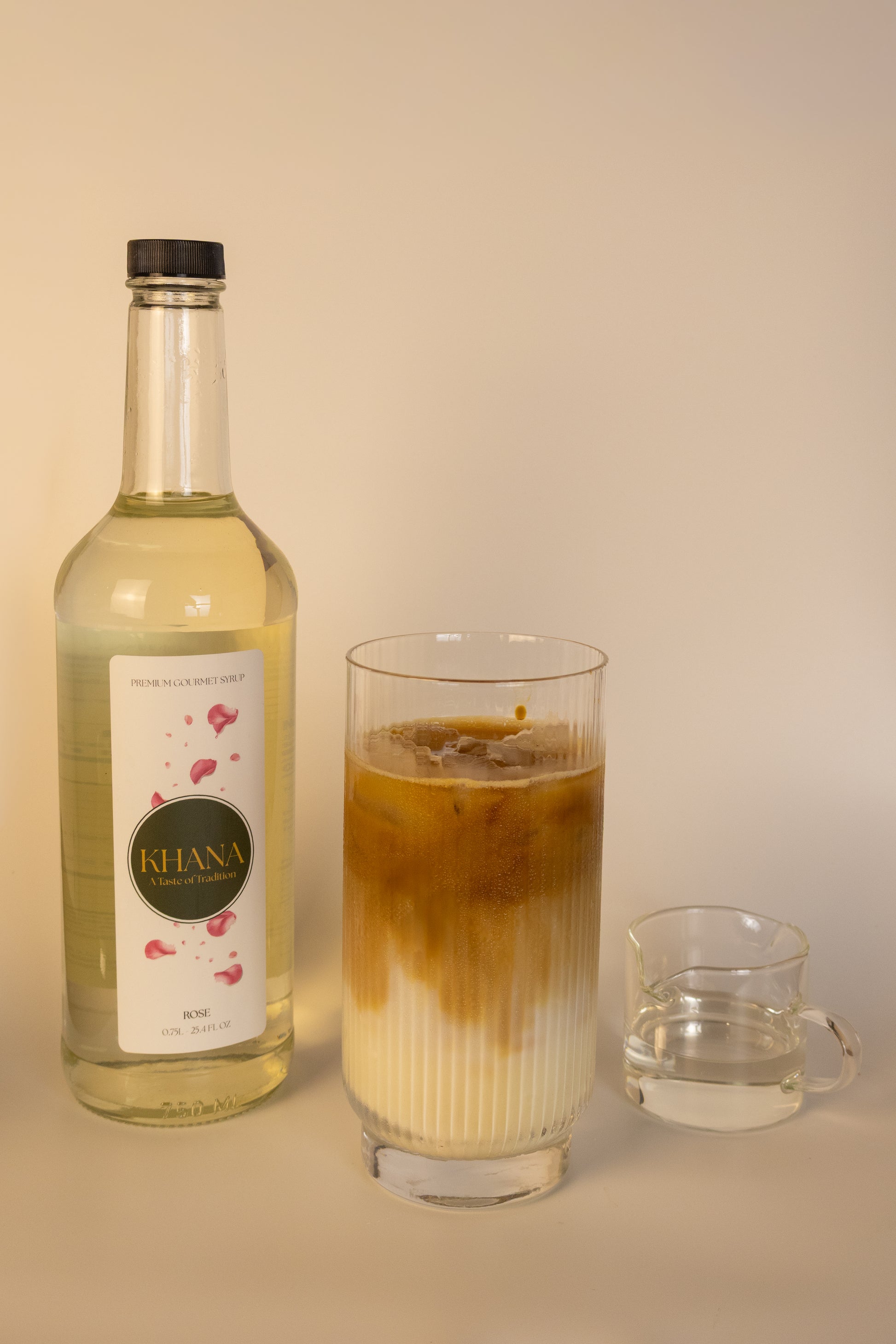Khana Rose Syrup 750mL bottle next to a glass of coffee latte and serving of syrup