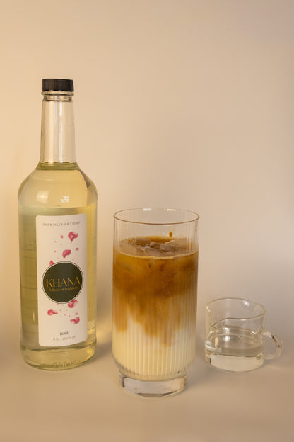 Khana Rose Syrup 750mL bottle next to a glass of coffee latte and serving of syrup