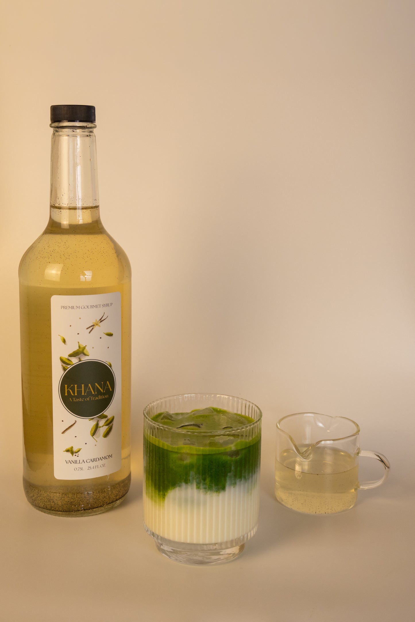 Khana Vanilla Cardamom Syrup 750mL bottle next to a glass of matcha and serving of syrup